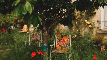 A tree with chairs underneath, surrounded by greenery and flowers.