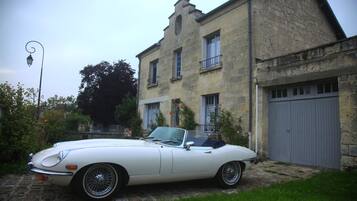 Un coche descapotable blanco estacionado frente a un edificio de piedra con un garaje.
