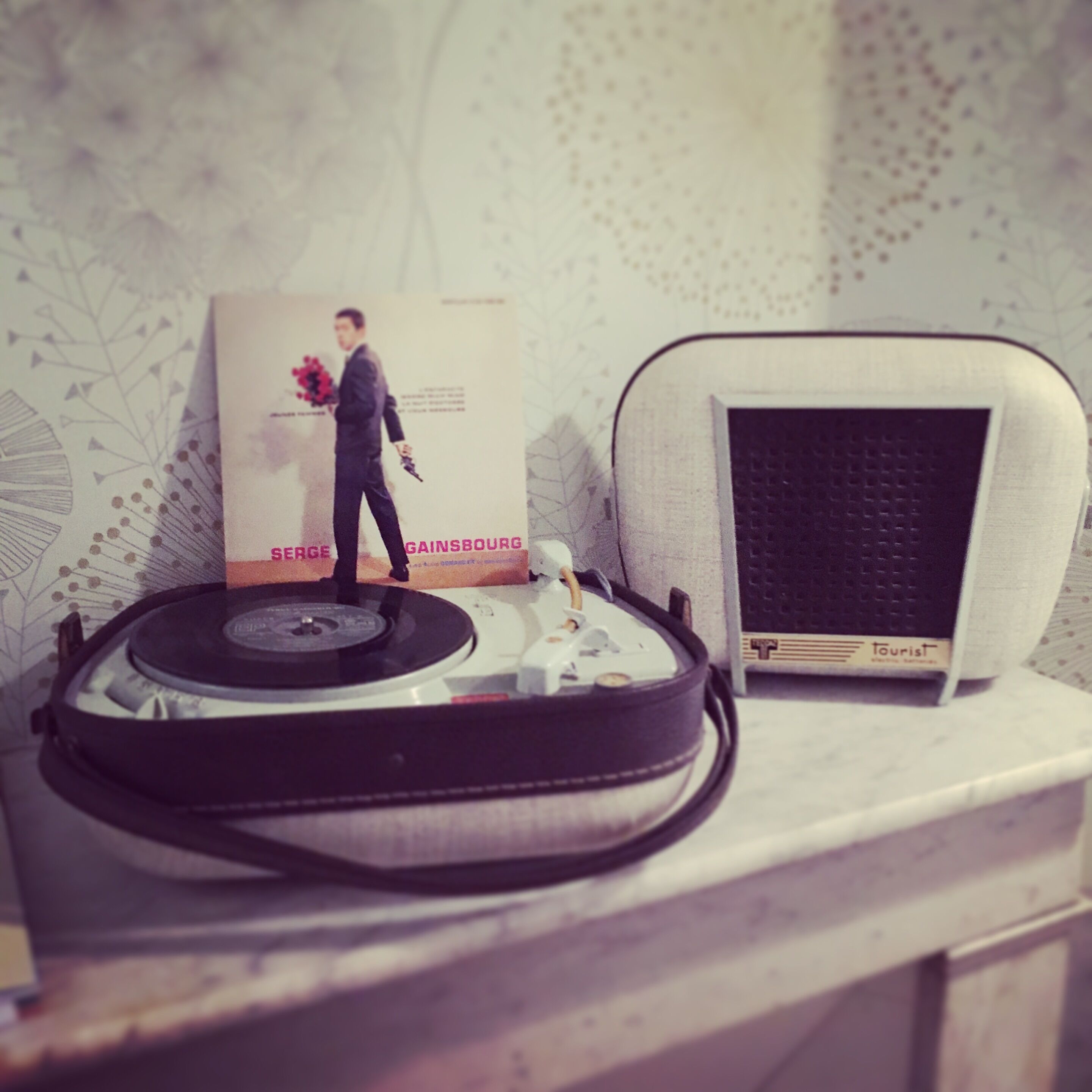 Tocadiscos con un disco, una radio antigua y un libro titulado 'Serge Gainsbourg Gainsbourg' sobre una estantería.