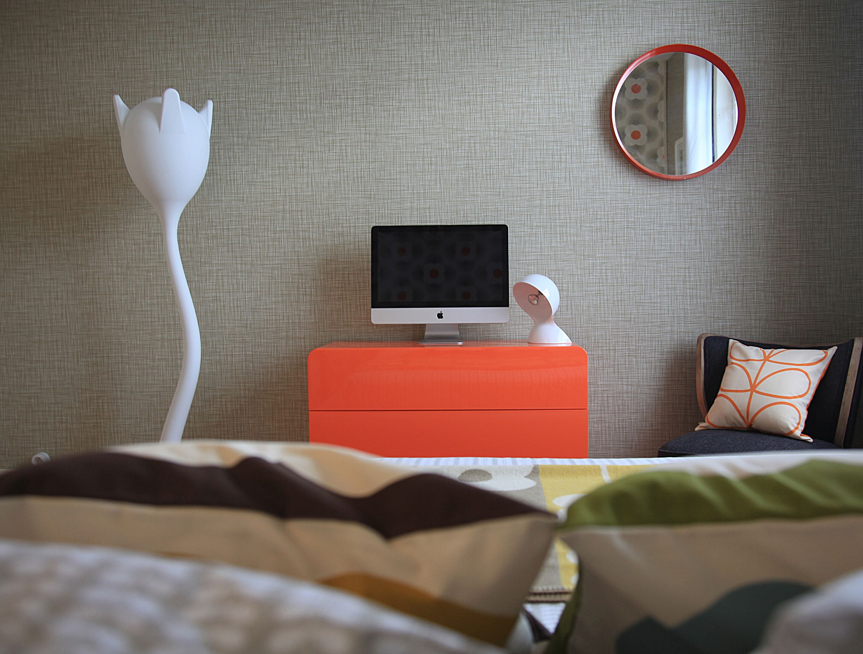 A hotel room with a bed, a desk with a computer, a mirror, and a wall with a textured pattern.