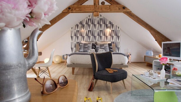A loft-style bedroom with a sloped ceiling, a bed with geometric-patterned bedding, a modern TV, and a glass coffee table. - Chez Ric et Fer (Coucy-le-Chateau-Auffrique)