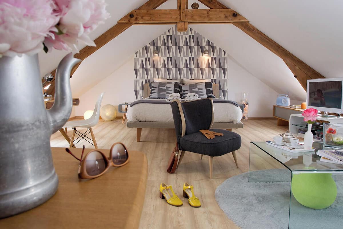 A loft-style bedroom with a sloped ceiling, a bed with geometric-patterned bedding, a modern TV, and a glass coffee table.
