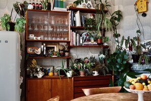 Une cuisine avec des étagères en bois, des plantes en pot, un panier de fruits et une horloge au mur.