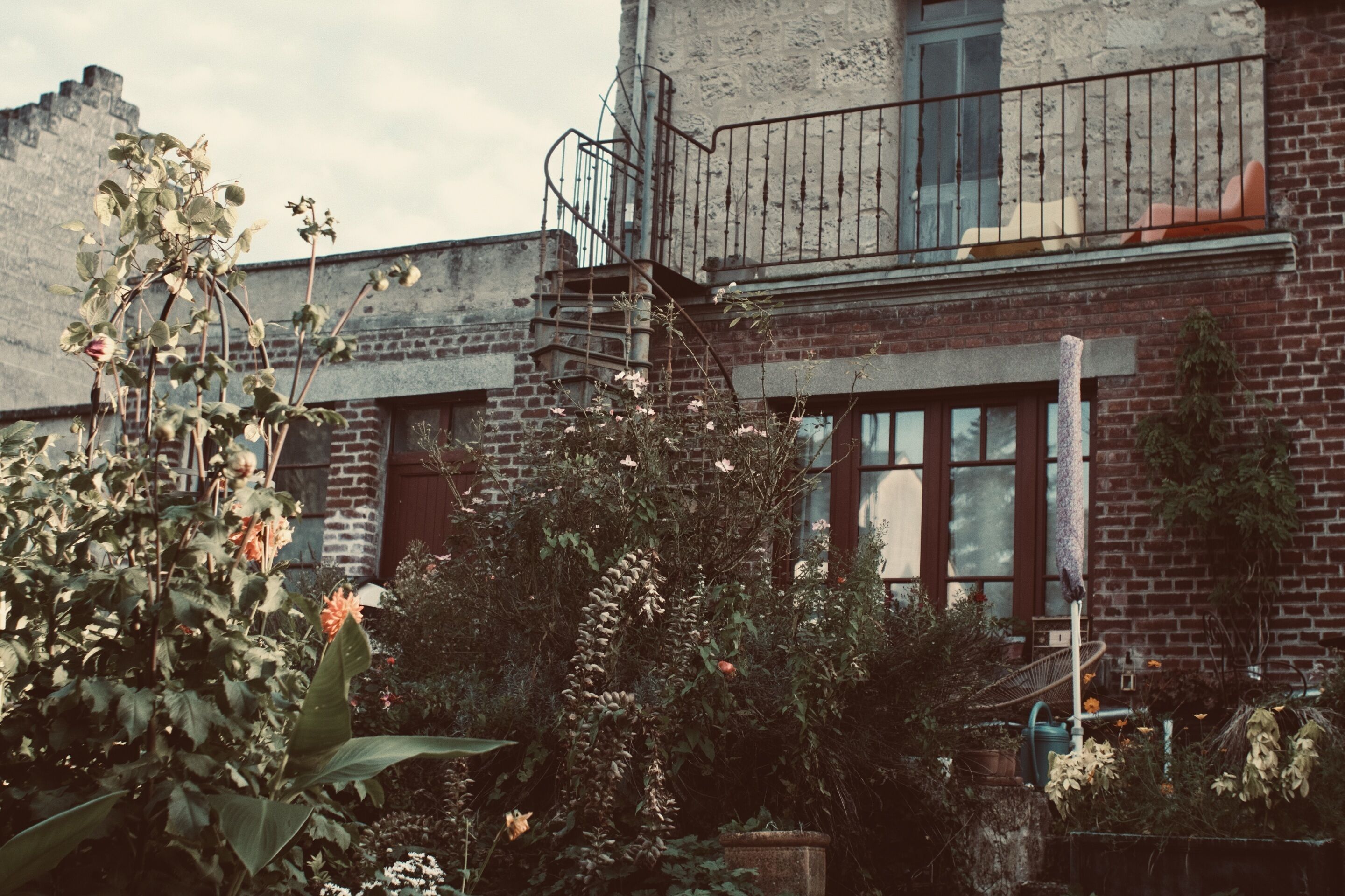 A brick building with a balcony, a window, and a garden area with various plants.