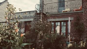 A brick building with a balcony, a window, and a garden area with various plants.
