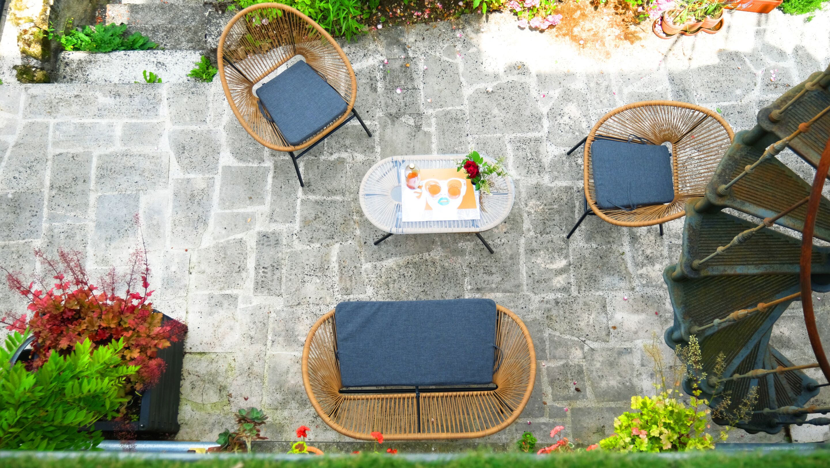 A patio with wicker furniture, a table, and potted plants.