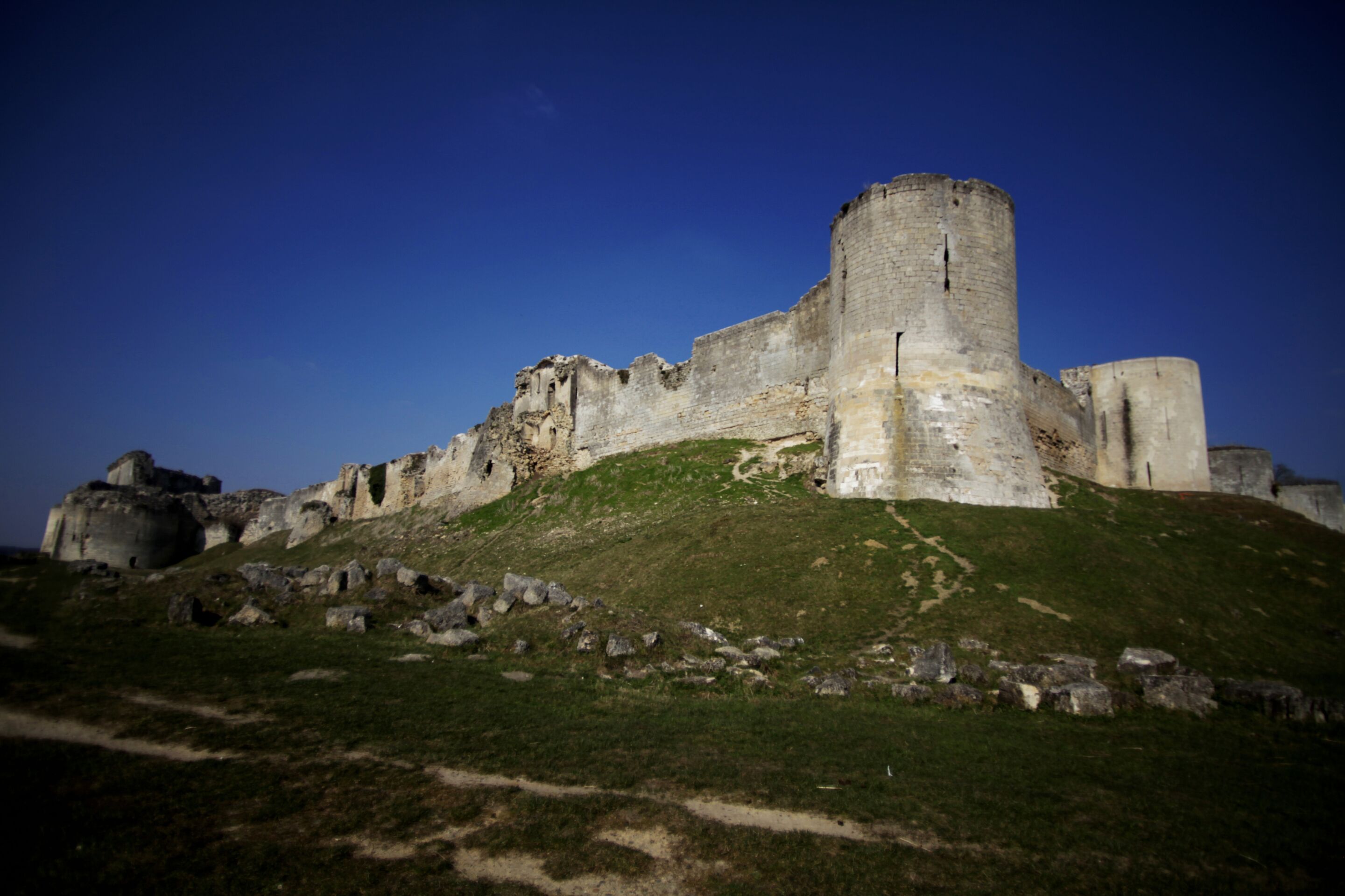 A historic castle with a prominent tower, surrounded by grassy terrain and rocky outcrops.