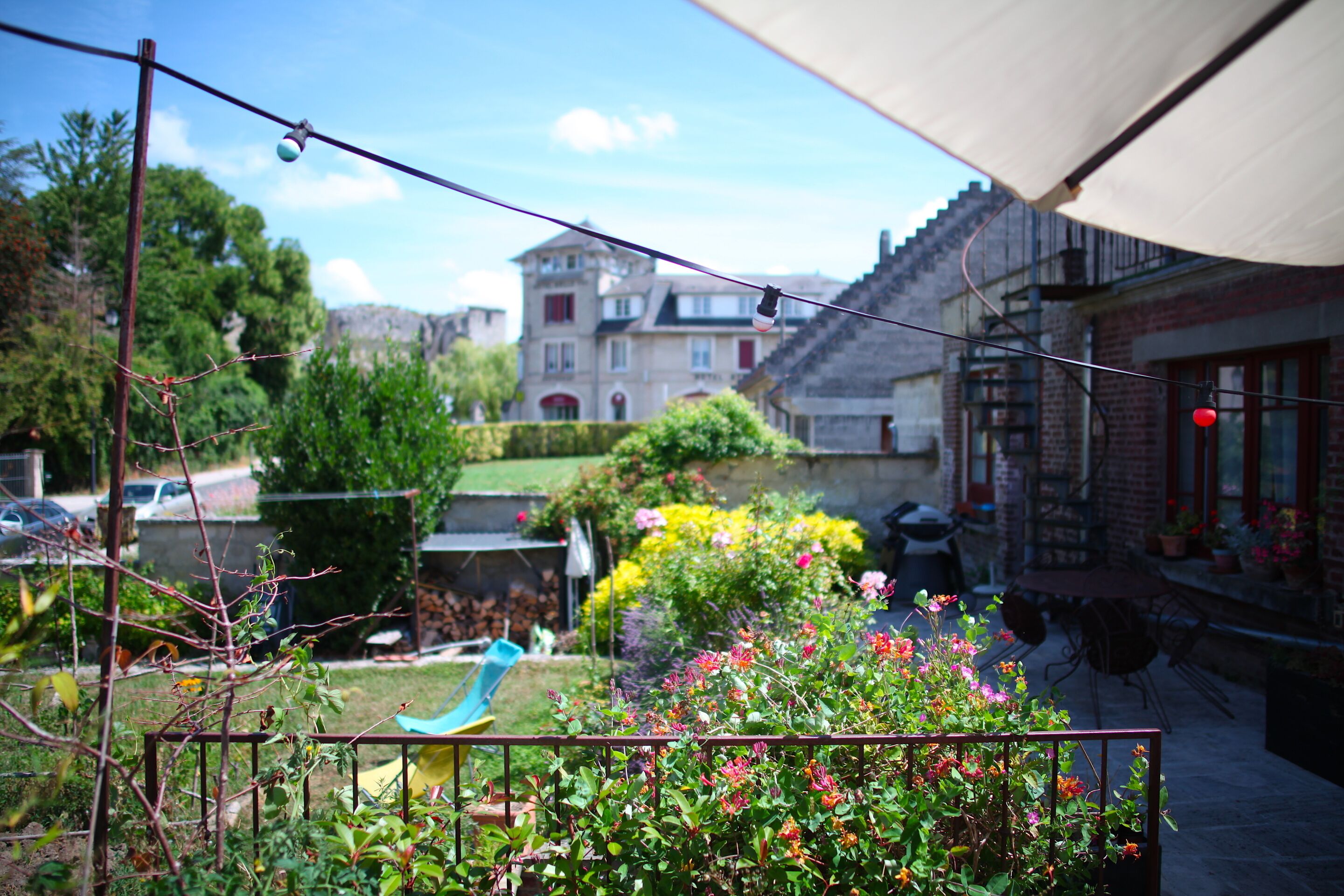 A garden with a metal fence, a blue chair, and a building with a red roof in the background.