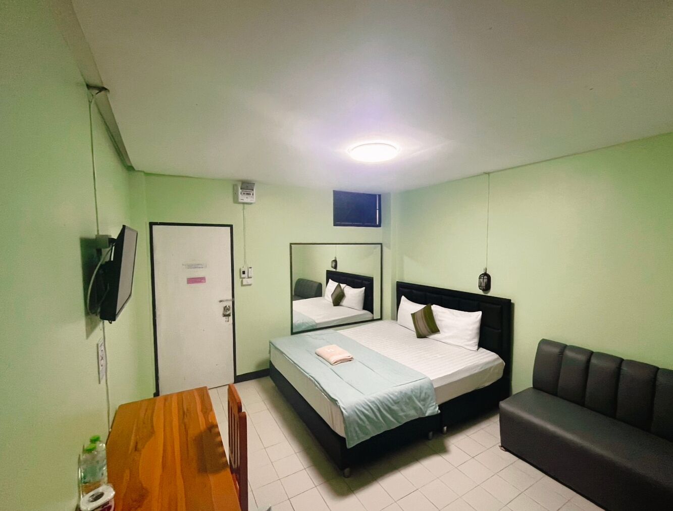 Een ruime, goed verlichte kamer met een bed, een bank, een bureau en een spiegel.