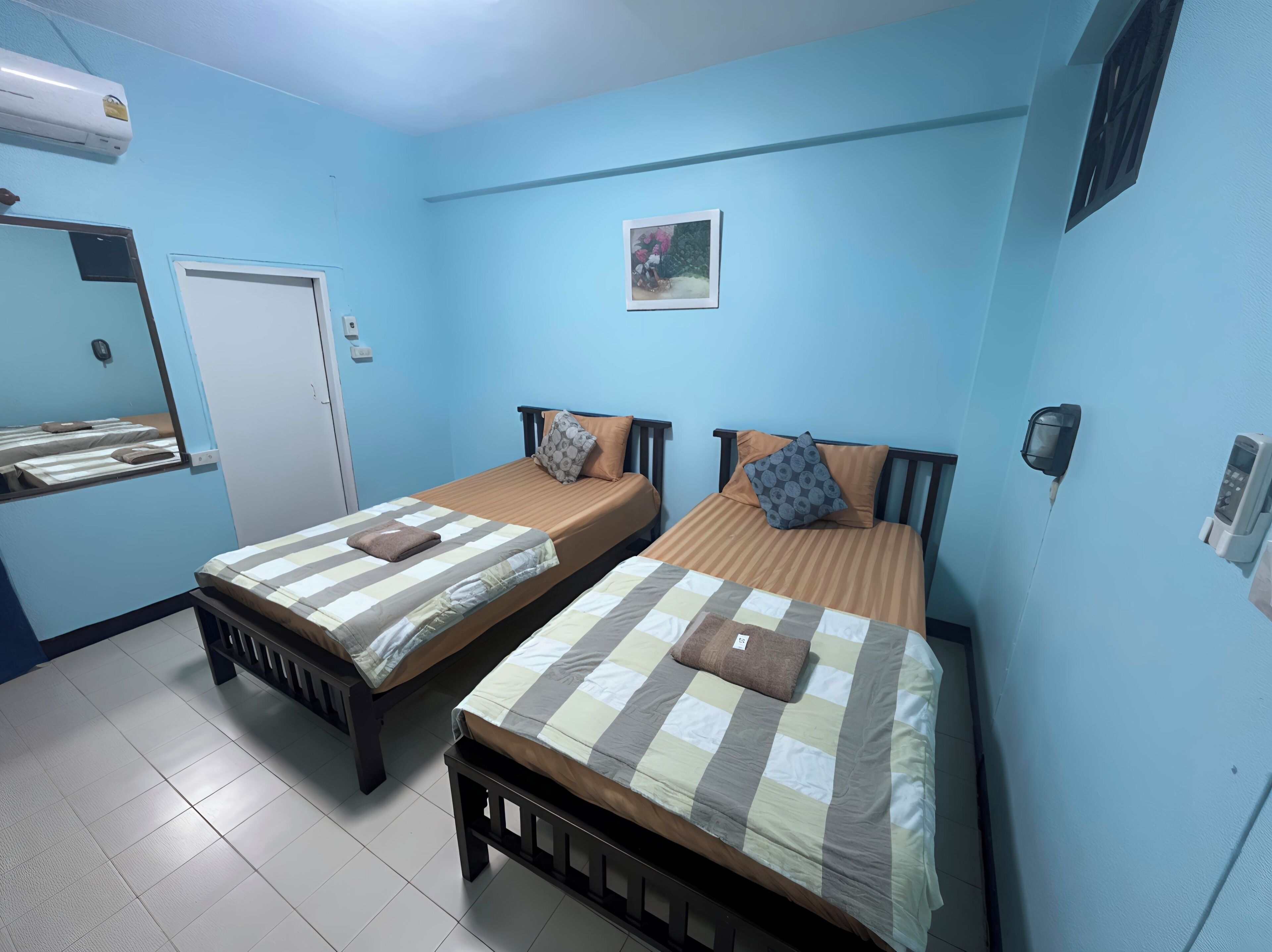 Una habitación con dos camas, una puerta, aire acondicionado instalado en la pared y un pequeño cuadro.
