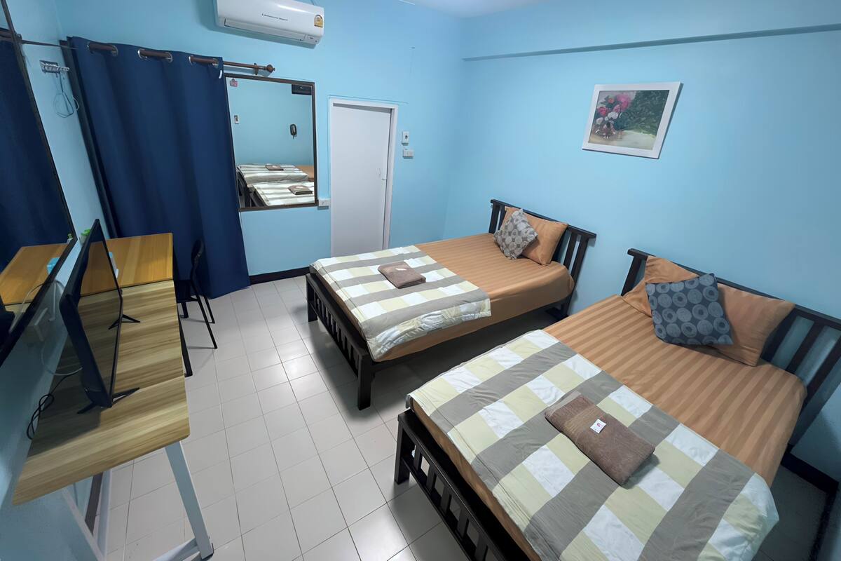A room with two beds, a desk, a mirror, and an air conditioner.