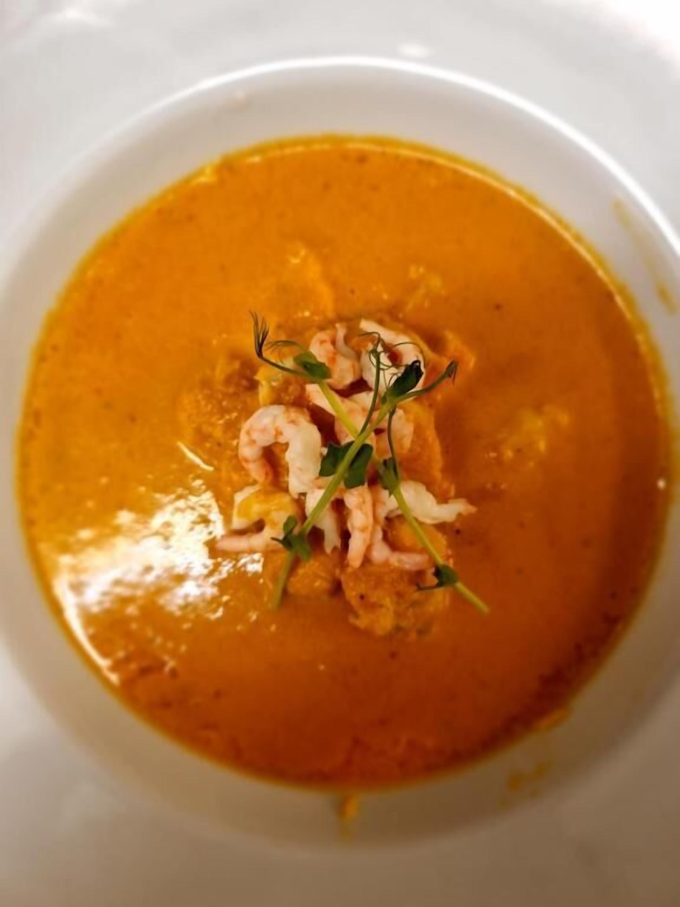Eine Schüssel Suppe mit Kräutern und Garnelen als Dekoration.