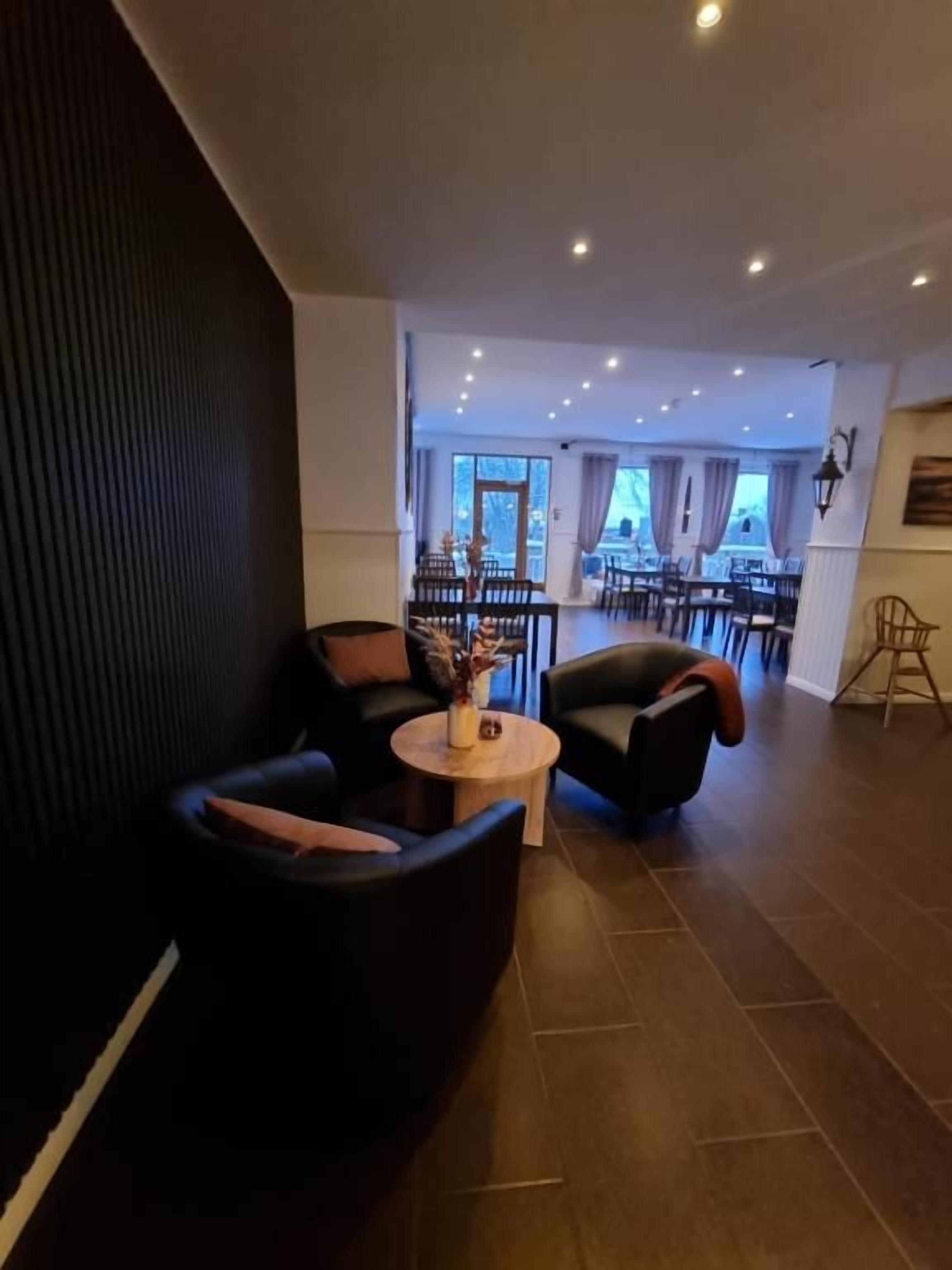 A modern interior with dark sofas, a round wooden table, and a view into a dining area with chairs and tables.