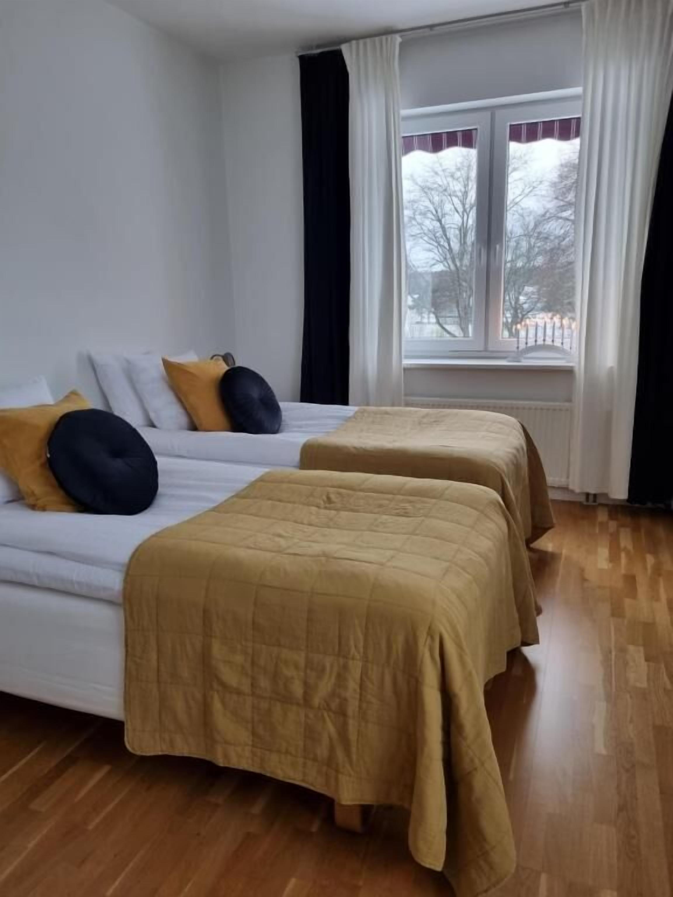 A room with two beds, a window with curtains, and a view of the outside.