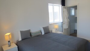 A bedroom with a large bed, two bedside tables with lamps, a window with a view, and a door leading to a bathroom. - Norrskedika hotell - Gamla Järnhandeln (Osthammar)