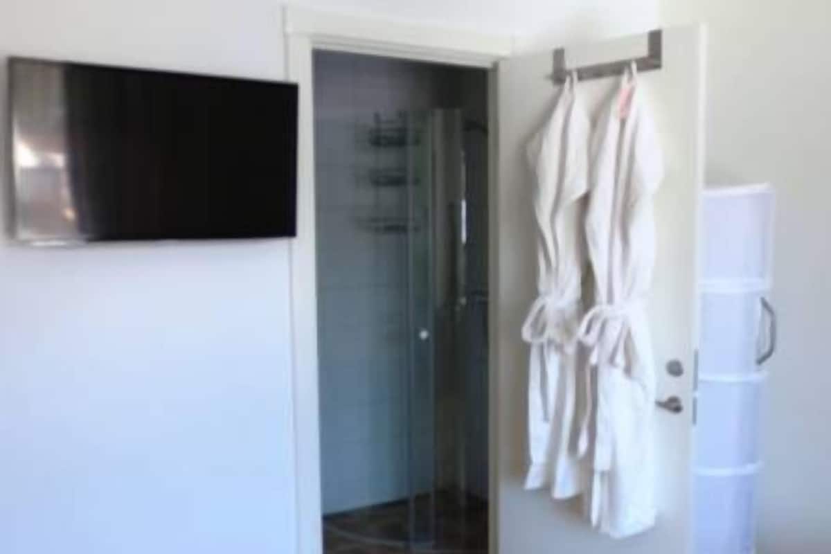 A room with a wooden floor, a glass shower enclosure, a white door with a towel rack, and a white cabinet.