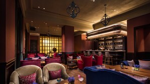 Amplia sala de estar con diversas opciones de asientos, incluyendo sillones y sofás, una zona de bar con estantes llenos de botellas, y un candelabro decorativo.