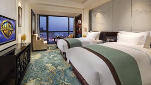 Habitación de hotel con dos camas, un ventanal amplio con vista a la ciudad, televisión y un minibar.