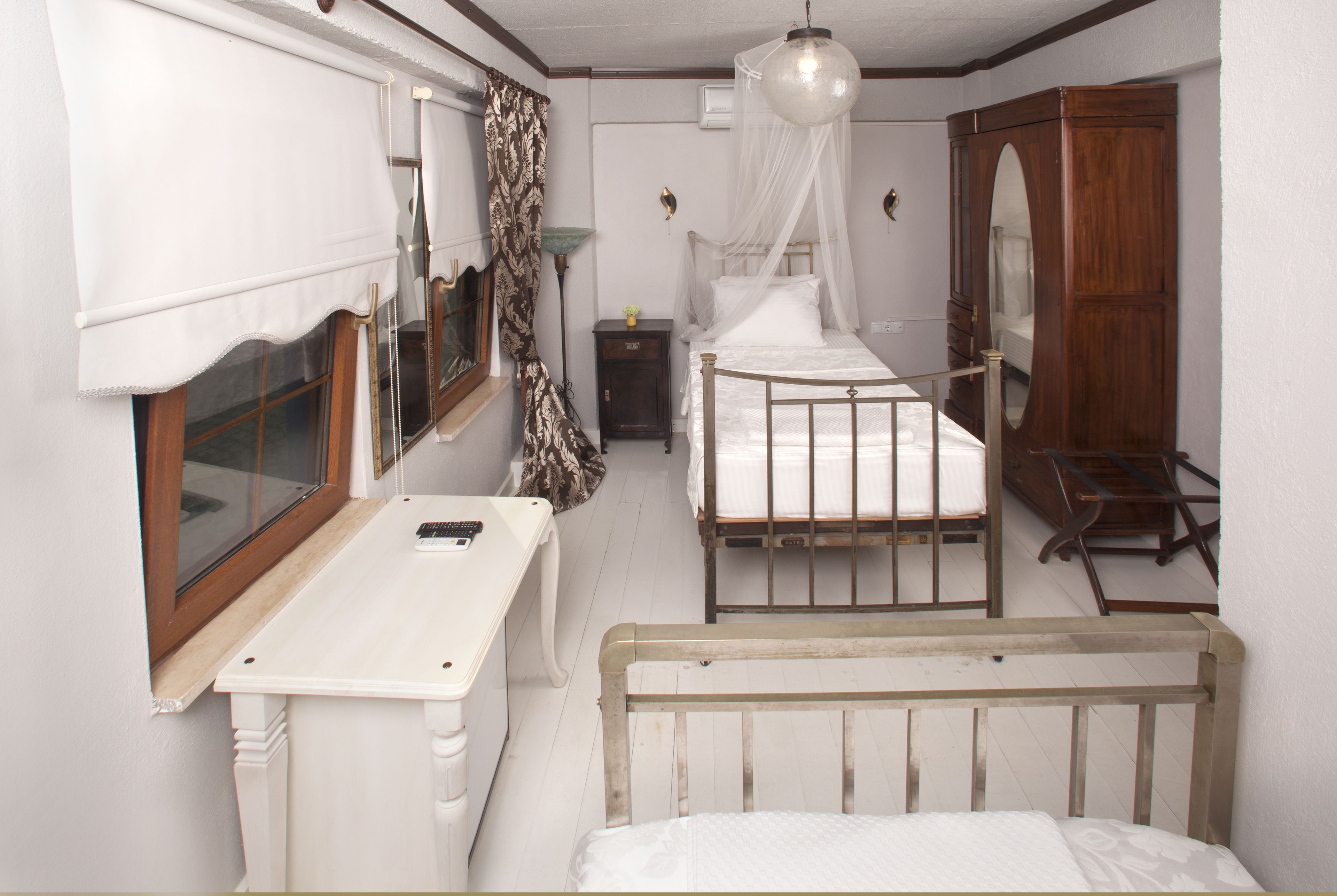Une chambre avec deux lits, une armoire en bois, une table de chevet, une fenêtre avec des rideaux et un luminaire suspendu.