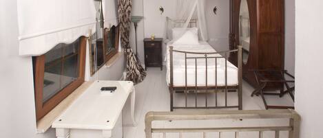 Une chambre avec deux lits, une armoire en bois, une table de chevet, une fenêtre avec des rideaux et un luminaire suspendu.