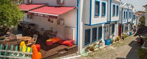 Um hotel com área de estar externa, toldo vermelho e fachada branca com detalhes azuis.