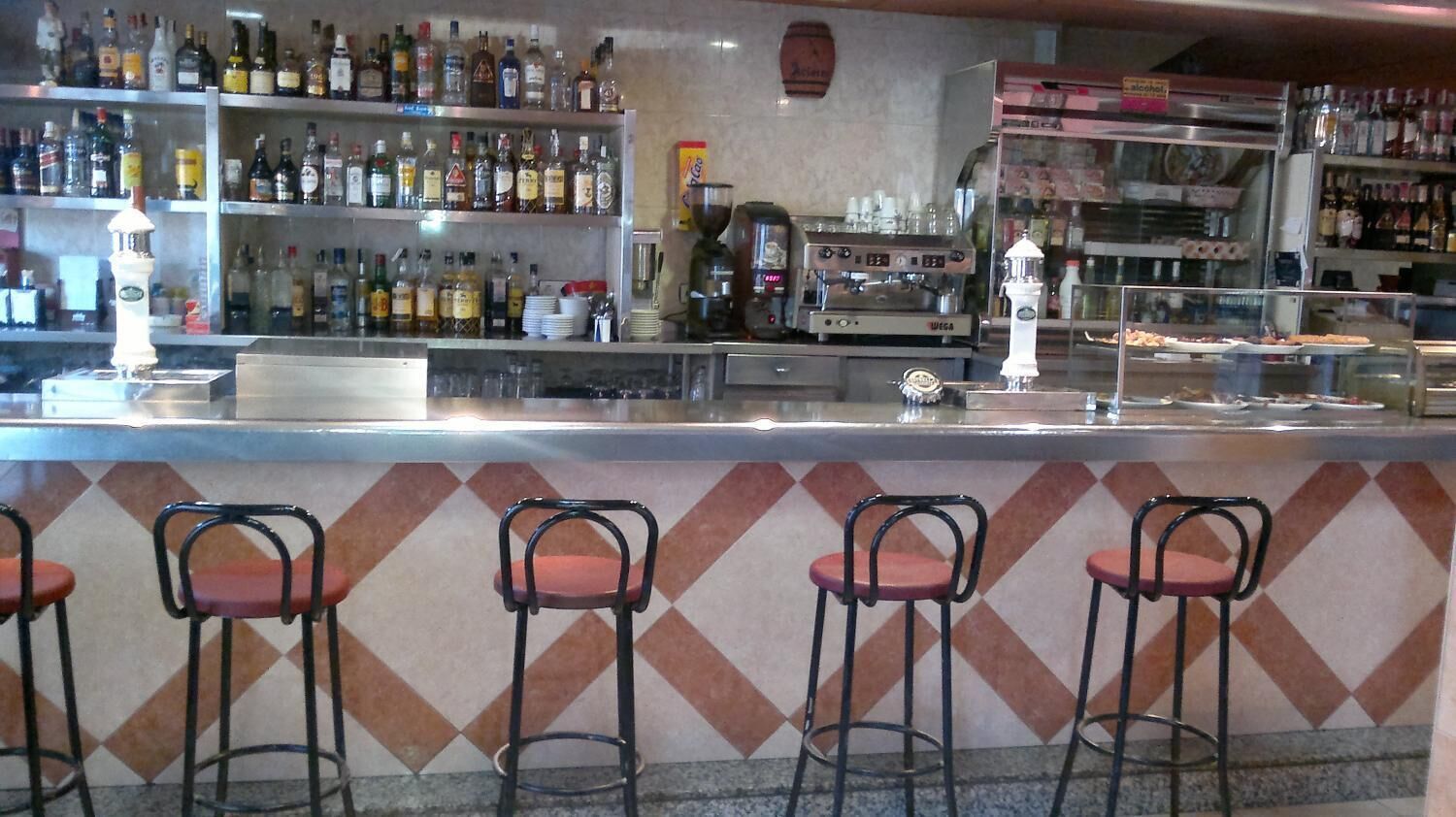 A bar area with a counter, stools, and shelves of various bottles.