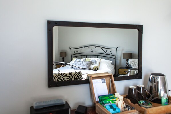 A hotel room with a bed, bedside tables, a mirror, and a tray with toiletries. - Oaklands Guest House (Weymouth)