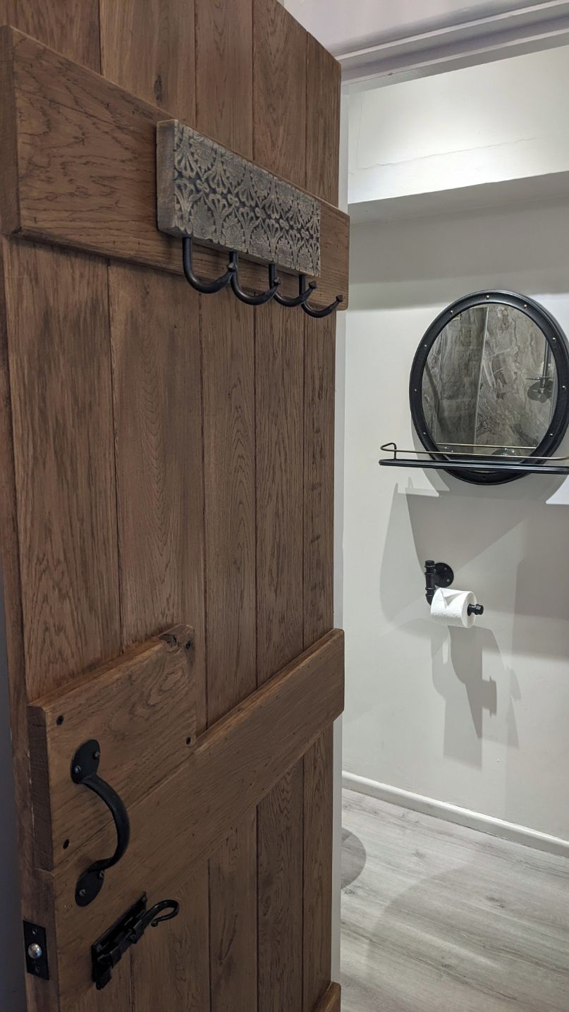 Une porte en bois avec une poignée en métal, un élément décoratif en métal au-dessus, et un miroir fixé au mur avec un distributeur de serviettes en dessous.