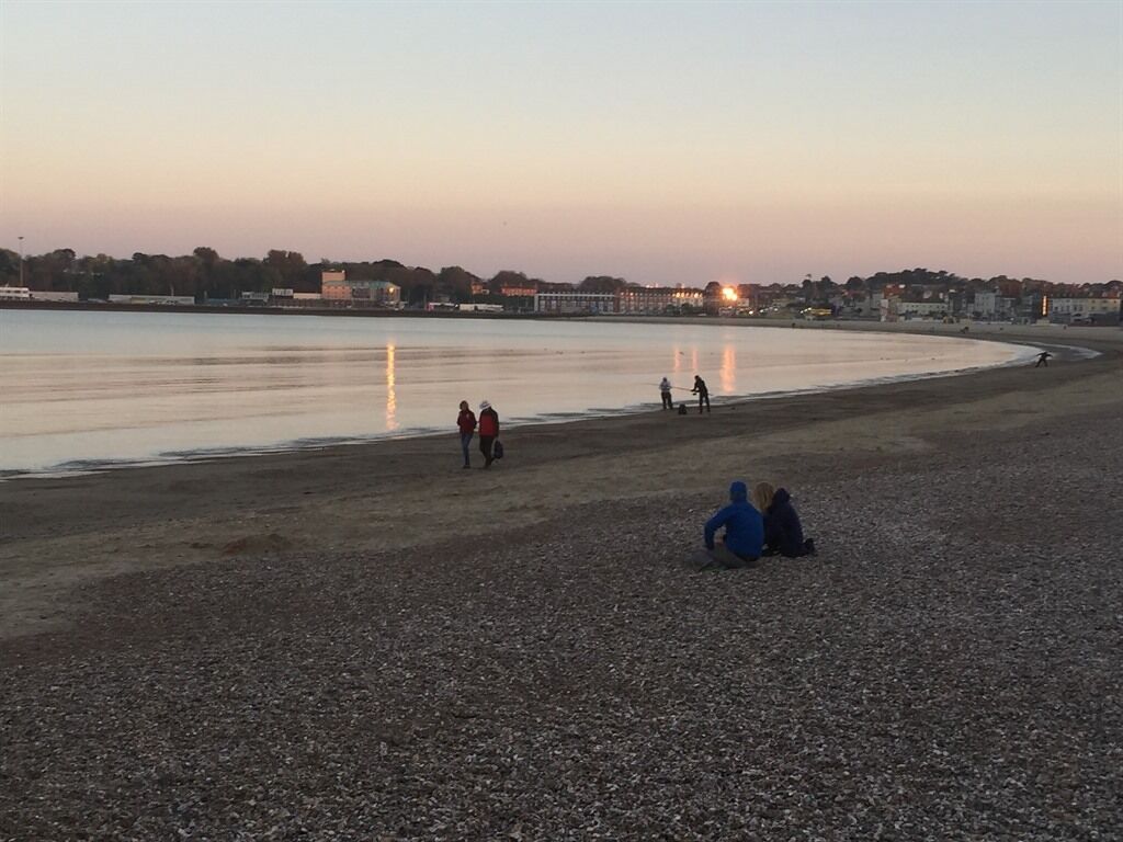 Une plage de galets où l’on voit des gens se promener et s’asseoir.
