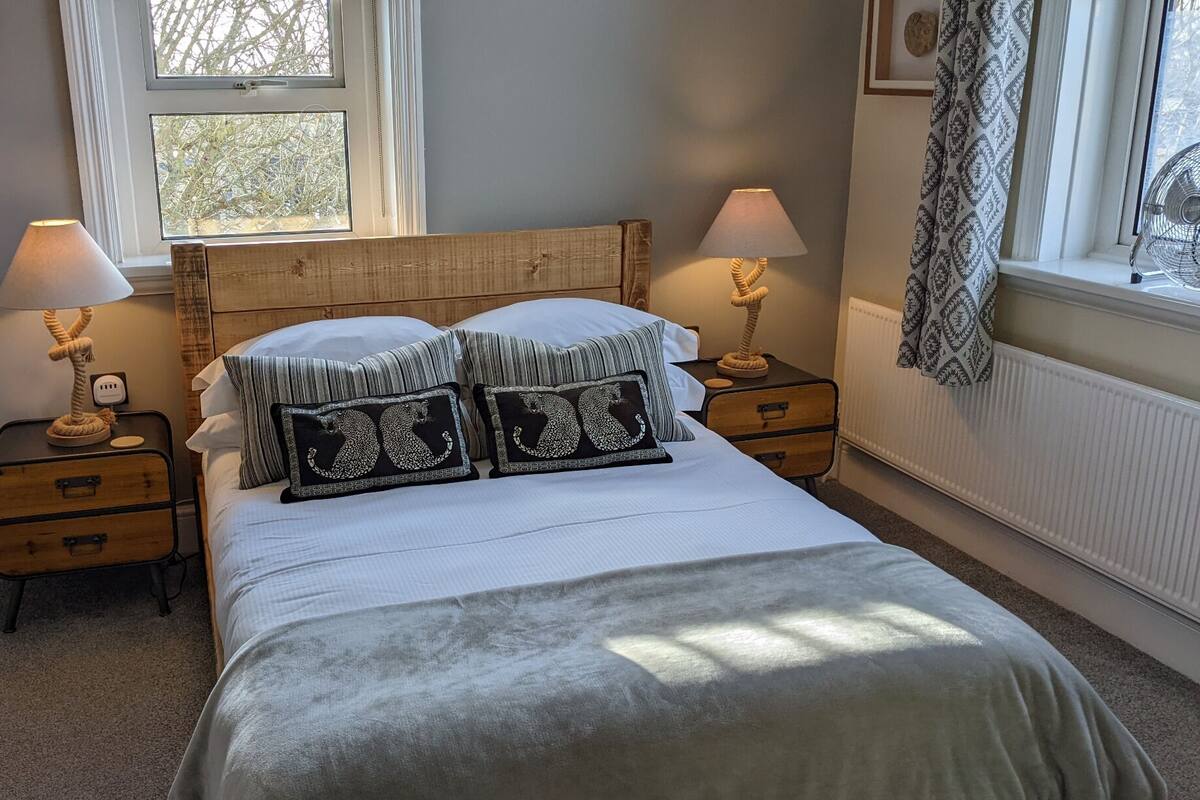 A bedroom with a bed, two bedside tables, a window, and a radiator.