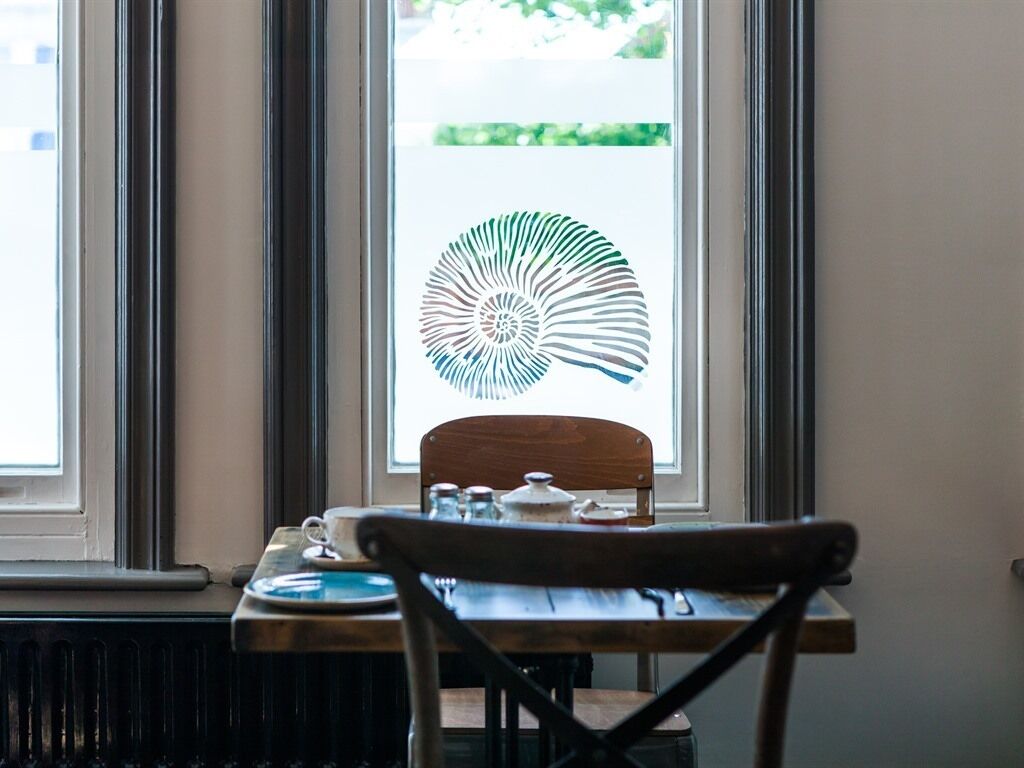 Un comedor con una mesa, sillas y un ventanal con película decorativa.