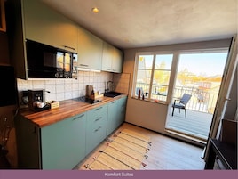 Una cocina compacta con encimera de madera, microondas integrado y ventana con vistas a un balcón.