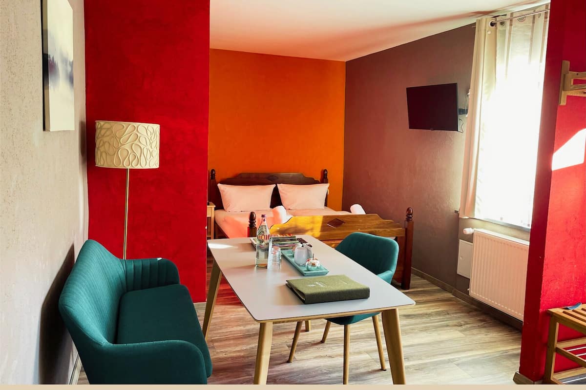 Quarto de hotel com cama, secretária e cadeira. Há uma janela com cortinas e um radiador.