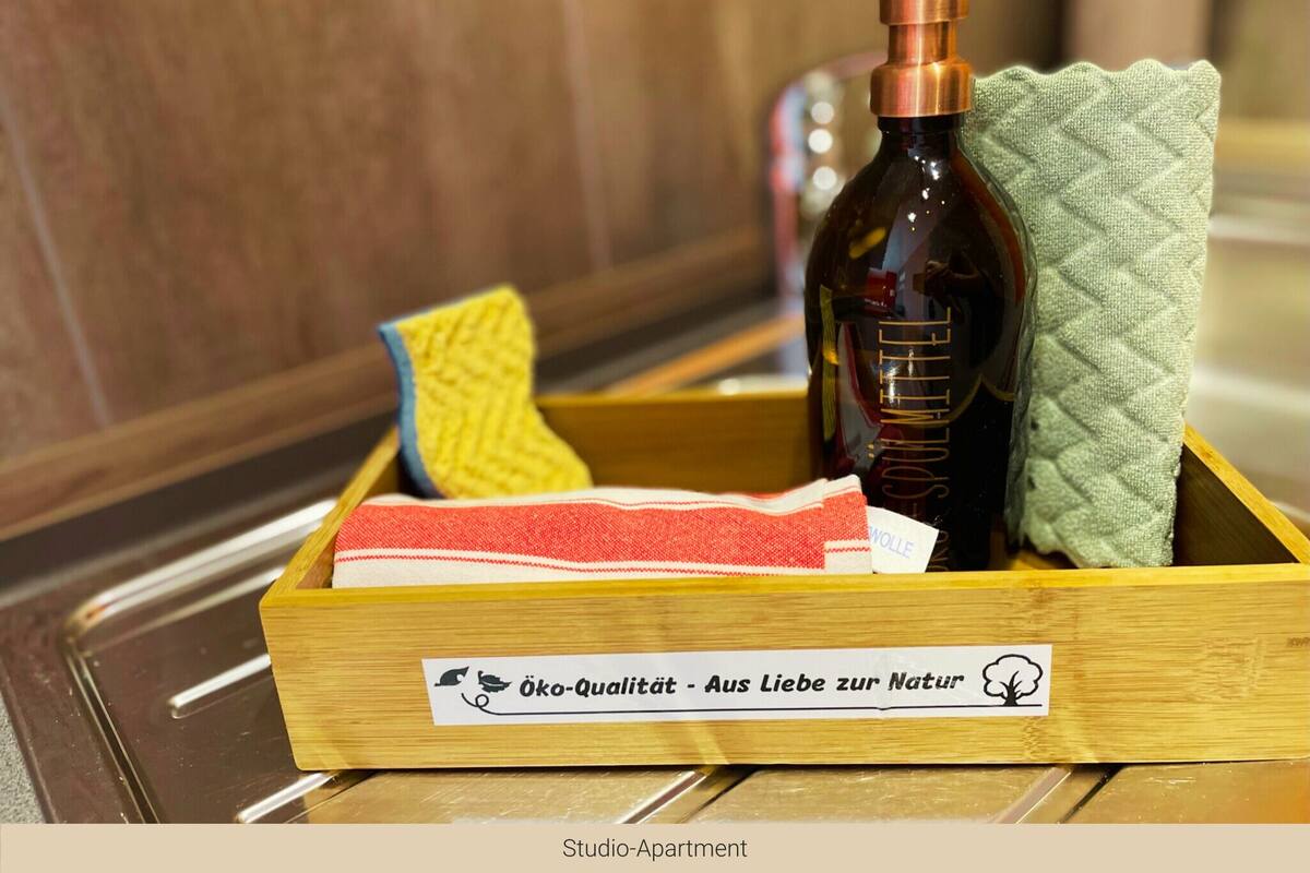 Eine Holzkiste mit einer Flasche Schwarze Melke, einem gelben Schwamm und einem grünen Handtuch, mit einem Etikett, das für Umweltqualität wirbt.