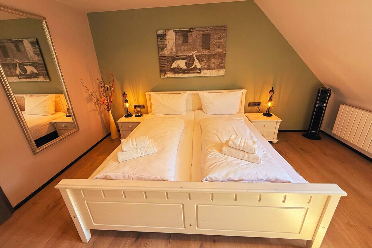 Ein Doppelbett mit weißer Bettwäsche, zwei Nachttische mit Lampen, ein Spiegel und ein Bild an der Wand.