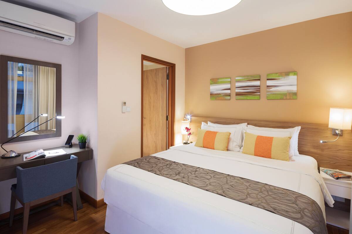 A hotel room with a bed, desk, chair, and a large window with curtains.