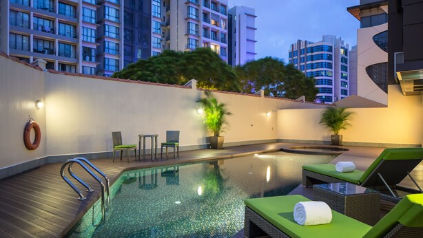 Una piscina sul tetto con sedie a sdraio e una vasca idromassaggio, circondata da edifici moderni e alberi.