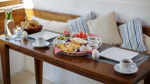 Uma mesa de café da manhã com diversos alimentos, uma xícara de café e um caderno sobre uma mesa de madeira em um quarto aconchegante com almofadas listradas.