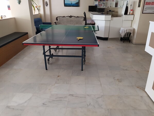 Una mesa de ping pong en una habitación con suelo de baldosas, un sofá y un televisor.