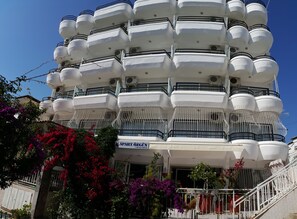 Un edificio de varios pisos con balcones, un letrero que dice "APART ÖZGÜN" y exuberante vegetación circundante.