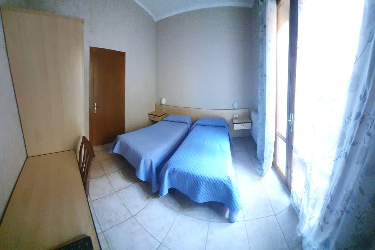 A bedroom with two beds, a wardrobe, a nightstand, and a window with curtains.