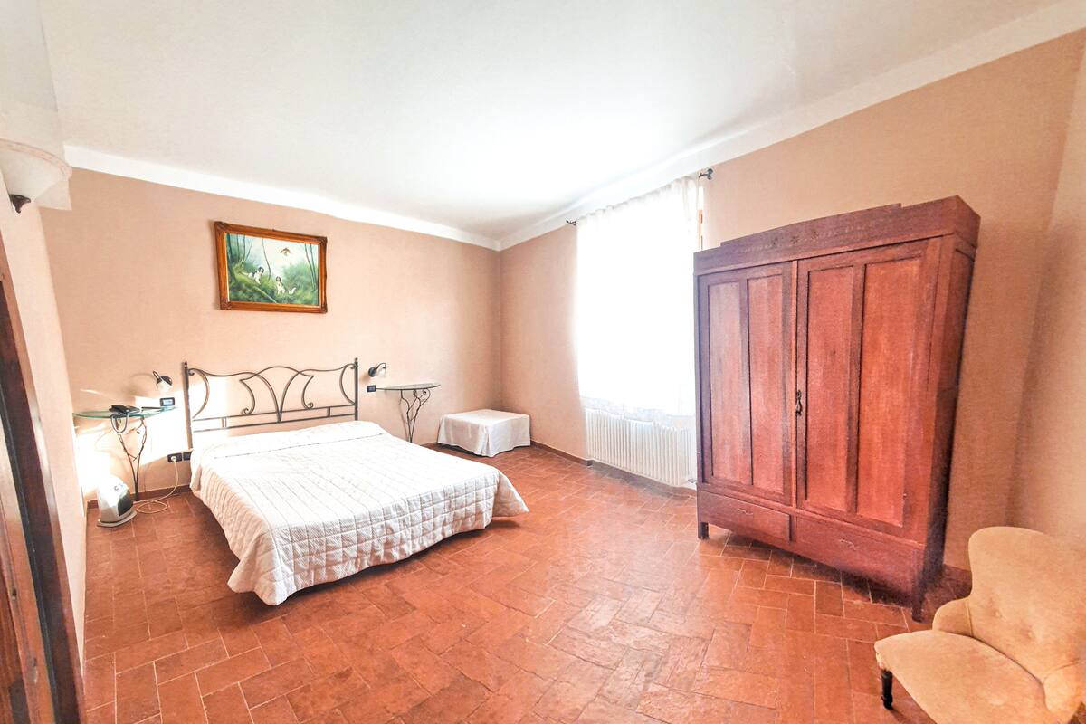 A bedroom with a bed, a wooden wardrobe, a chair, a radiator, and a painting on the wall.