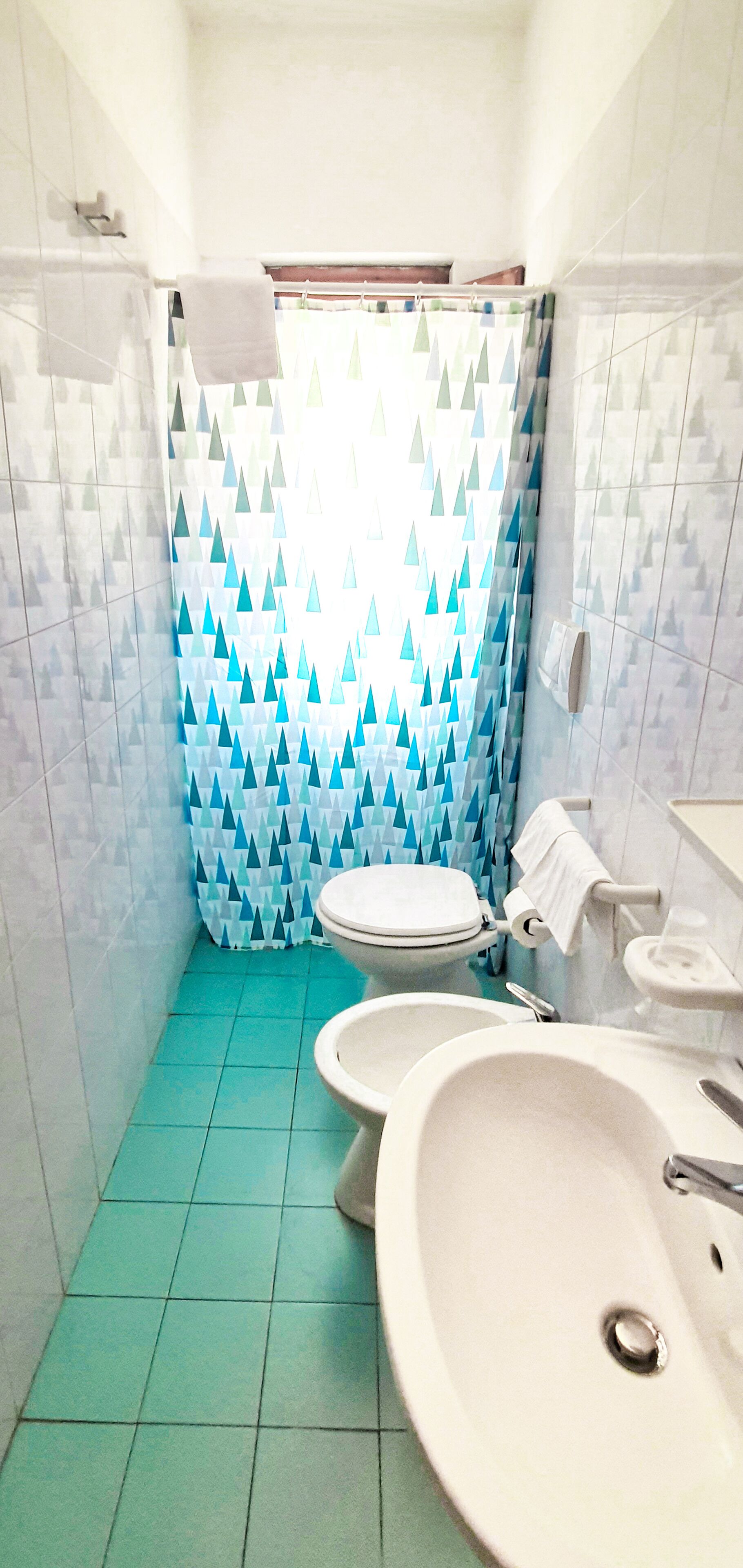 Ein Badezimmer mit zwei Toiletten, einem Waschbecken und einer Duschvorhang mit geometrischem Muster.