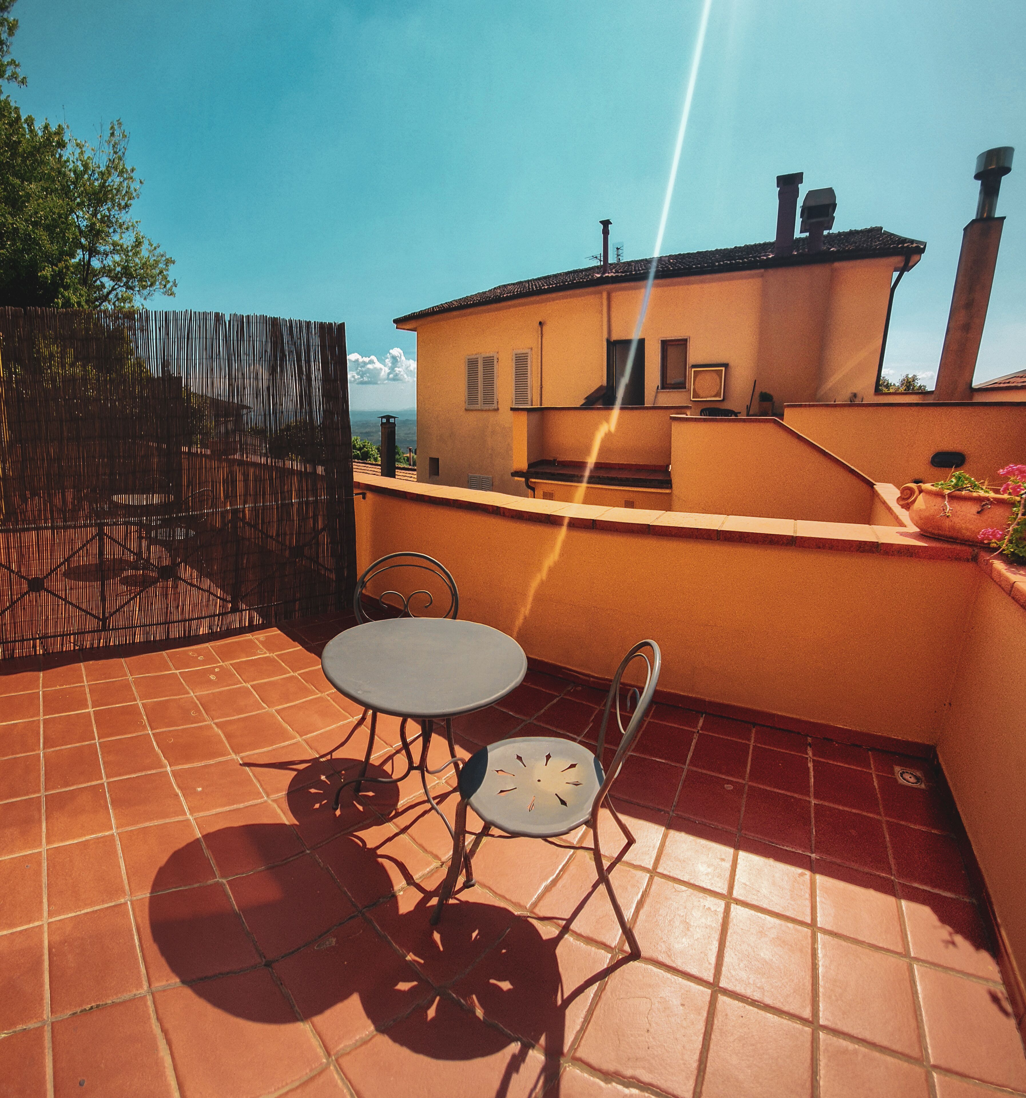 Eine Terrasse mit Tisch und Stühlen, Blick auf ein Gebäude und ein klarer Himmel.