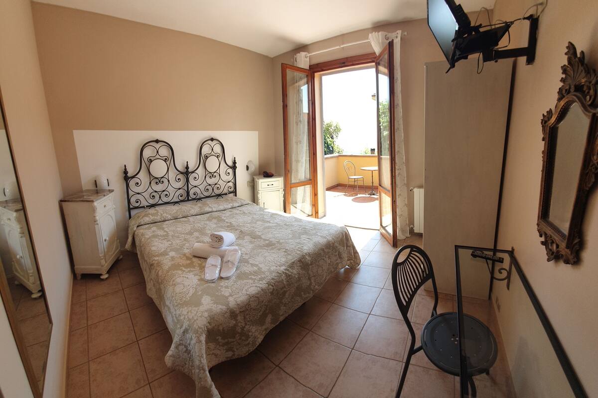 A bedroom with a bed, a chair, a TV, and a balcony.