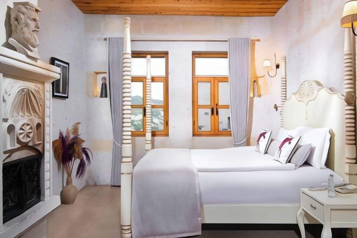 A bedroom with a bed, a fireplace, a window with curtains, and a wall-mounted lamp.