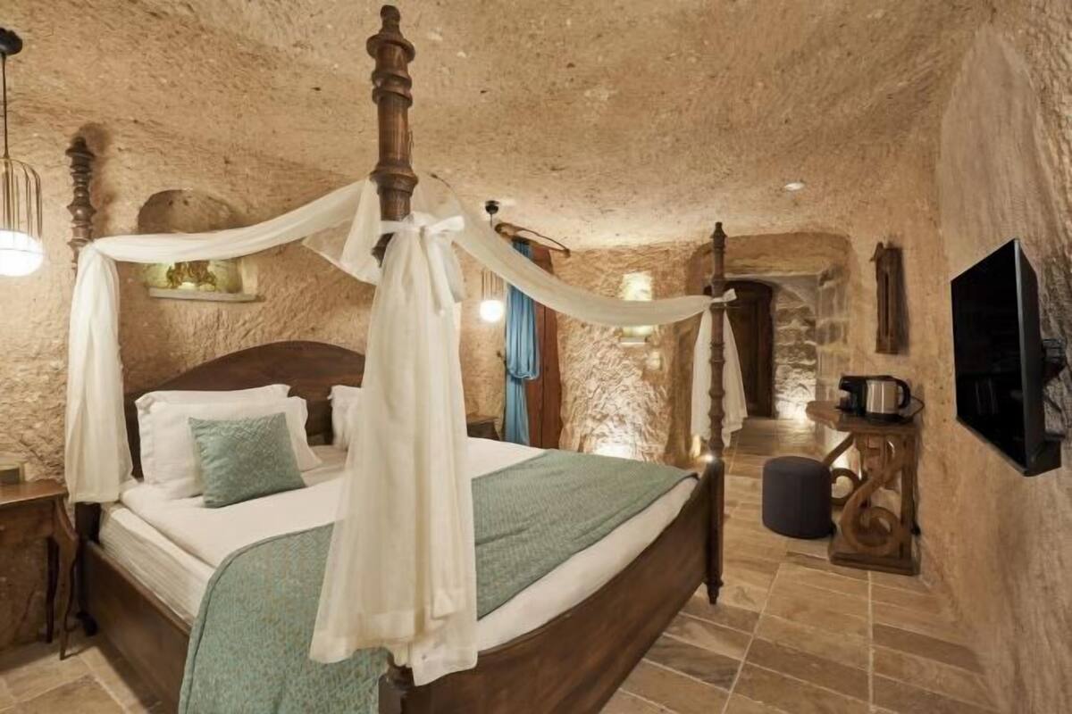 A four-poster bed with a canopy, a television, and a stone wall.
