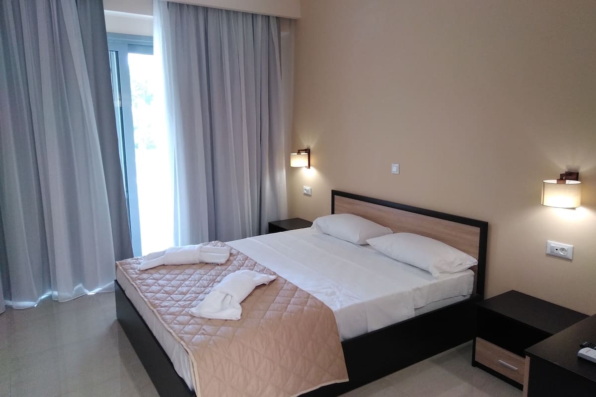 Quarto de hotel com cama, duas mesas de cabeceira e uma janela com cortinas.