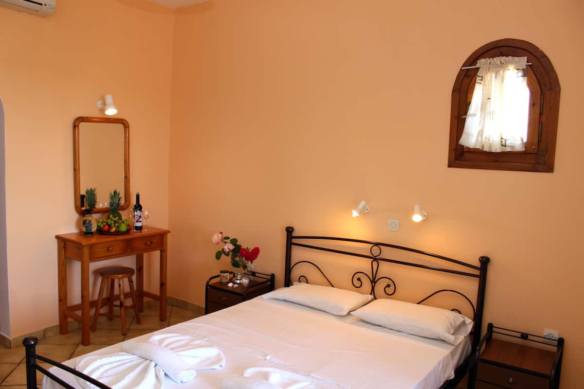 Quarto com cama, escrivaninha de madeira, cadeira, mesa de cabeceira, espelho e janela com cortinas.