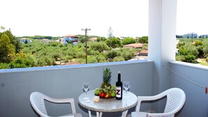 Een balkon met een tafel gedekt voor twee personen, inclusief een fles wijn, een schaal met fruit en twee glazen.